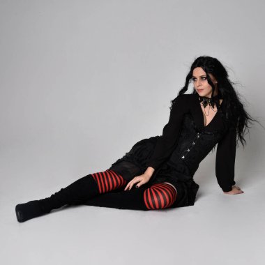 Siyah Victoria tarzı cadı kostümü giyen, stüdyo arka planında hareketli, hareketli, siyah saçlı bir kadının tam boy portresi..