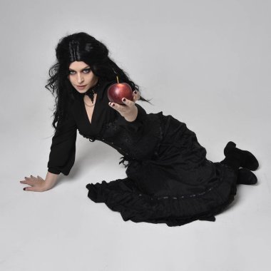 Siyah Victoria tarzı cadı kostümü giyen, yerde yatan, ölü gibi uyuyan, stüdyo arka planında soyutlanmış koyu renk saçlı kadının tam boy portresi..