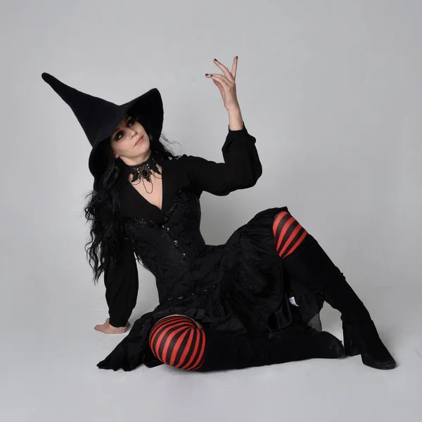 全长的黑发女子肖像 身穿黑色维多利亚式的女巫服装 手部有手势动作 背景在工作室 — 图库照片