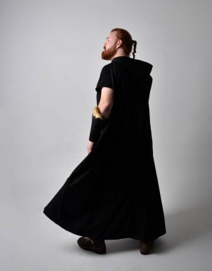  Ortaçağ Viking 'i giyen kızıl saçlı adamın portresi koyu renk pelerinli fantezi kostümüne ilham verdi. Stüdyo arka planına izole edilmiş bir büyü yapar gibi hareketli poz veriyor..
