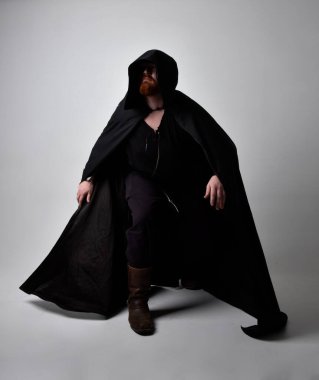  portrait of red haired man wearing medieval viking inspired fantasy costume with dark cloak. Standing pose  with gestural hand movements as if casting a spell, isolated  against studio background. clipart