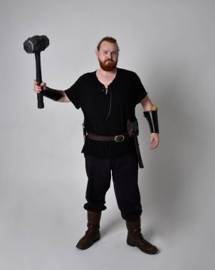  Ortaçağ Viking 'i giymiş kızıl saçlı adamın portresi fantezi kostümünden esinlenmiştir. Silah olarak bir çekiç tutan hareketli pozlar, stüdyo arka planında izole edilmiş..
