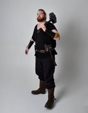  Ortaçağ Viking 'i giymiş kızıl saçlı adamın portresi fantezi kostümünden esinlenmiştir. Silah olarak bir çekiç tutan hareketli pozlar, stüdyo arka planında izole edilmiş..