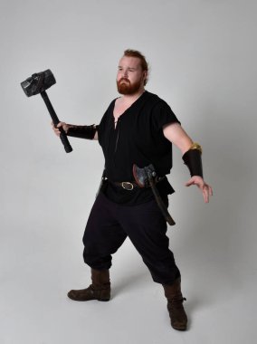  Ortaçağ Viking 'i giymiş kızıl saçlı adamın portresi fantezi kostümünden esinlenmiştir. Silah olarak bir çekiç tutan hareketli pozlar, stüdyo arka planında izole edilmiş..