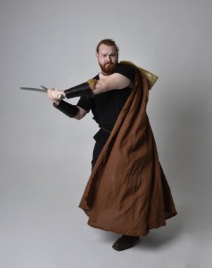  portrait of red haired man wearing medieval viking inspired fantasy costume, holding a long sword weapon. Isolated against studio background clipart