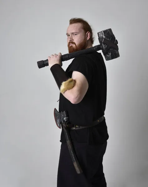 红头发男人穿着中世纪维京风格的奇幻服装的肖像 举着锤子作为武器的站立姿势 与工作室背景隔离 — 图库照片