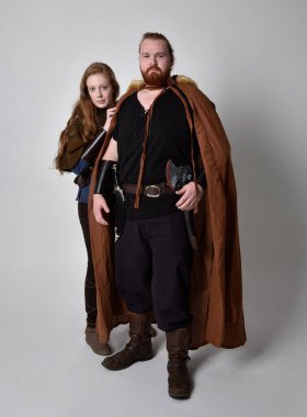 Kızıl saçlı bir çiftin tam boy portresi, ortaçağ Viking 'i giyen bir adam ve kadın ilham verici fantezi kostümleri, ayakta duruş, beyaz stüdyo arka planında izole edilmiş..