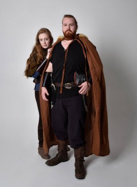 Full length portrait of red haired couple, man and woman wearing medieval viking inspired fantasy costumes, standing pose, isolated on white studio background. clipart