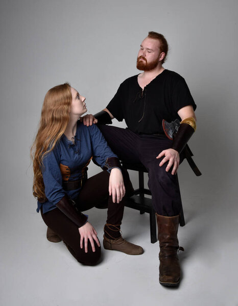 Full length  portrait of red haired  couple, man and woman wearing medieval viking inspired fantasy costumes, sitting poses, isolated on white  studio background.