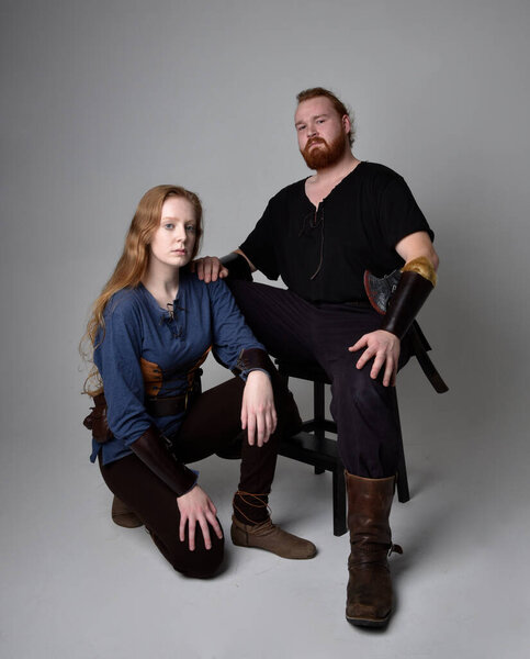 Full length  portrait of red haired  couple, man and woman wearing medieval viking inspired fantasy costumes, sitting poses, isolated on white  studio background.