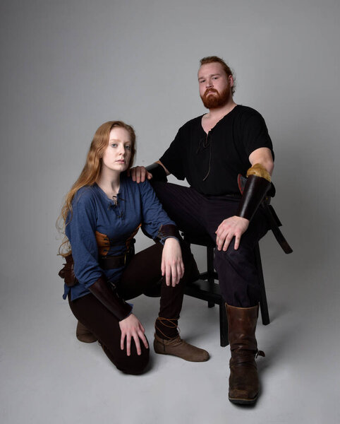 Full length  portrait of red haired  couple, man and woman wearing medieval viking inspired fantasy costumes, sitting poses, isolated on white  studio background.