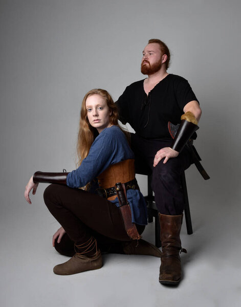 Full length  portrait of red haired  couple, man and woman wearing medieval viking inspired fantasy costumes, sitting poses, isolated on white  studio background.