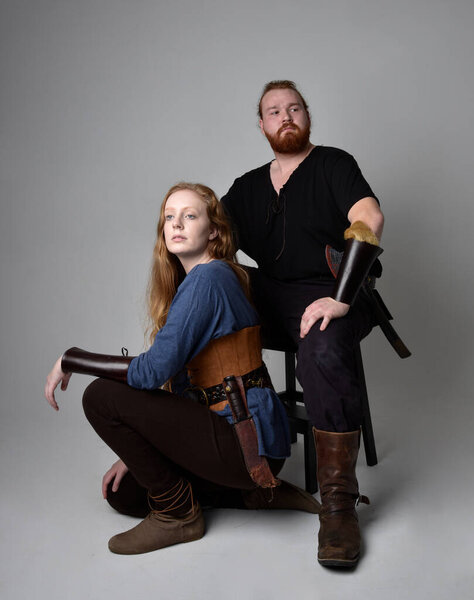 Full length  portrait of red haired  couple, man and woman wearing medieval viking inspired fantasy costumes, sitting poses, isolated on white  studio background.