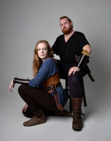 Full length  portrait of red haired  couple, man and woman wearing medieval viking inspired fantasy costumes, sitting poses, isolated on white  studio background.