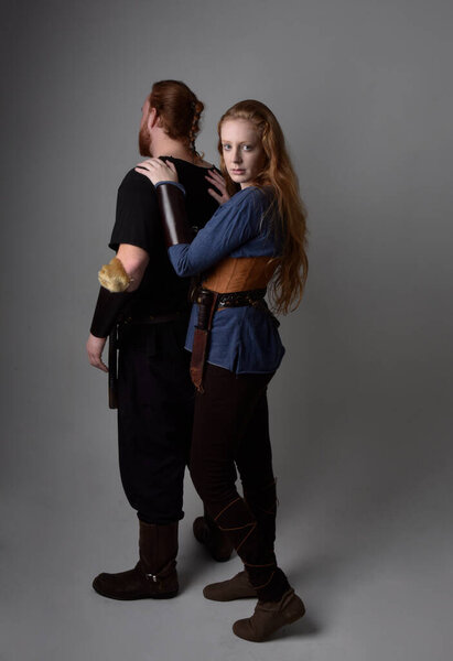 Full length  portrait of red haired  couple, man and woman wearing medieval viking inspired fantasy costumes, standing romantic intimate poses, isolated on white  studio background.