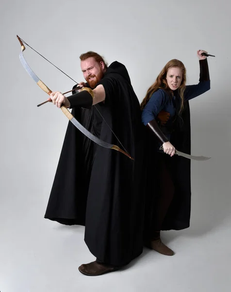 红头发夫妇的全长肖像 男人和女人穿着中世纪维京风格的奇幻服装 站在战斗的姿势上 手持弓箭和长剑 隔离在白色的工作室背景下 — 图库照片