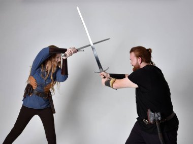 Kızıl saçlı bir çiftin tam boy portresi, ortaçağ Viking 'i giymiş bir adam ve kadın ilham verici fantezi kostümleri, duruş pozisyonu kılıç tutuş, beyaz stüdyo arka planında izole edilmiş.
