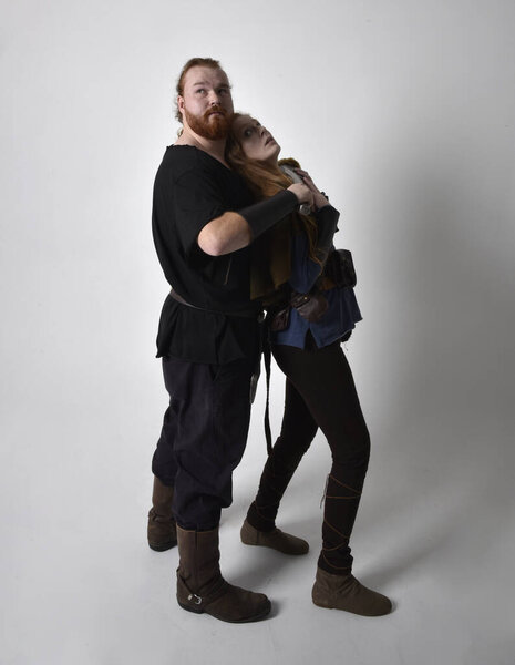 Full length  portrait of red haired  couple, man and woman wearing medieval viking inspired fantasy costumes, standing fighting pose holding  sword weapons, isolated on white  studio background.