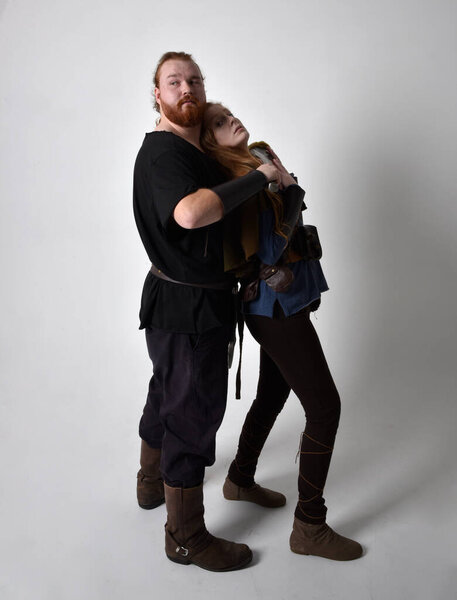 Full length  portrait of red haired  couple, man and woman wearing medieval viking inspired fantasy costumes, standing fighting pose holding  sword weapons, isolated on white  studio background.