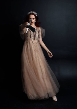 Peri tanrıçası kostümü gibi kremalı bir fantezi elbisesi giyen kızıl saçlı kızın tam boy portresi. Stüdyonun arka planında izole edilmiş zarif hareketli duruş..