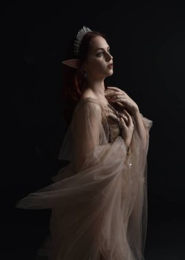 close up portrait of red haired  girl wearing a creamy fantasy gown like a fairy goddess costume.  isolated on dark studio background. clipart