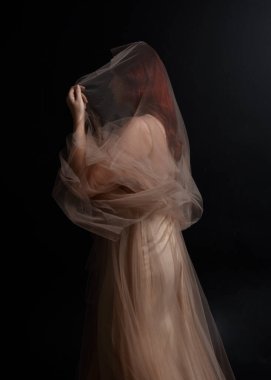 Peri tanrıçası kostümü gibi kremalı bir fantezi elbisesi giyen kızıl saçlı kızın tam boy portresi. Stüdyonun arka planında izole edilmiş zarif hareketli duruş..