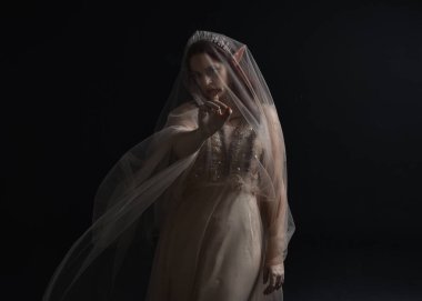 Peri tanrıçası kostümü gibi kremalı bir fantezi elbisesi giyen kızıl saçlı kızın tam boy portresi. Stüdyonun arka planında izole edilmiş zarif hareketli duruş..