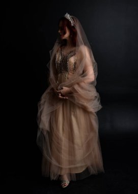 Peri tanrıçası kostümü gibi kremalı bir fantezi elbisesi giyen kızıl saçlı kızın tam boy portresi. Stüdyonun arka planında izole edilmiş zarif hareketli duruş..