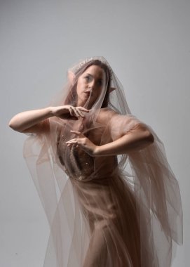portrait of red haired  girl wearing a creamy fantasy gown and flowing veil fabric, like a fairy goddess costume.  standing  pose with elegant gestural hands, isolated on light studio background. clipart