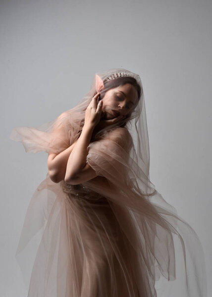 portrait of red haired  girl wearing a creamy fantasy gown and flowing veil fabric, like a fairy goddess costume.  standing  pose with elegant gestural hands, isolated on light studio background.