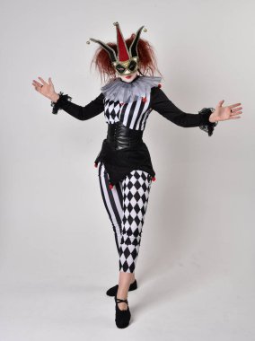 Siyah beyaz palyaço kostümü giyen kızıl saçlı bir kızın uzun bir portresi. Tiyatral sirk karakteri. Stüdyo arka planında izole edilmiş poz.