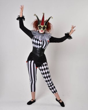 Siyah beyaz palyaço kostümü giyen kızıl saçlı bir kızın uzun bir portresi. Tiyatral sirk karakteri. Stüdyo arka planında izole edilmiş poz.