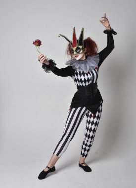 Siyah beyaz palyaço kostümü giyen kızıl saçlı bir kızın uzun bir portresi. Tiyatral sirk karakteri. Stüdyo arka planında izole edilmiş poz.