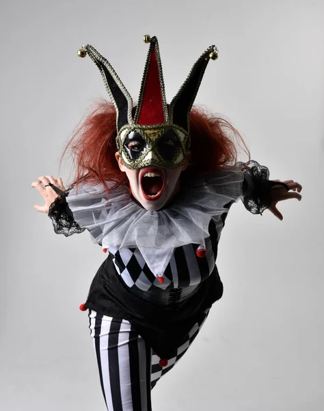 穿着黑白相间小丑小丑小丑装束的红头发女孩的近照 戏剧化的马戏团角色 独立于工作室背景的站立姿势 — 图库照片