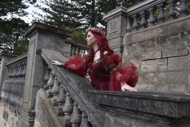  Kızıl saçlı, çekici gotik siyah dantelli balo elbisesi giyen güzel bir kadın modelin portresi. Merdiveni olan bir masal kalesinde poz vermek. 