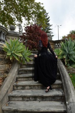  Kızıl saçlı, çekici gotik siyah dantelli balo elbisesi giyen güzel bir kadın modelin portresi. Merdiveni olan bir masal kalesinde poz vermek. 
