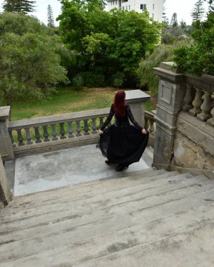  Kızıl saçlı, çekici gotik siyah dantelli balo elbisesi giyen güzel bir kadın modelin portresi. Merdiveni olan bir masal kalesinde poz vermek. 