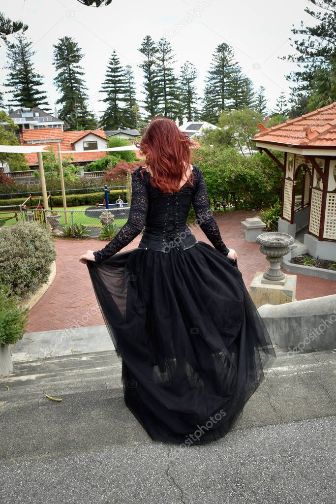  portrait of pretty  female model with red hair wearing glamorous gothic black lace ballgown.  Posing in a fairytale castle location with staircases 