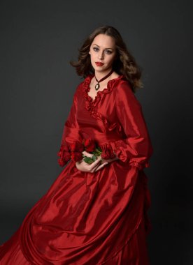  Kızıl saçlı güzel bir kadın modelin portresi Viktorya dönemi kırmızı balo elbisesi giyiyor. Huysuz, karanlık bir geçmişi olan poz vermek..