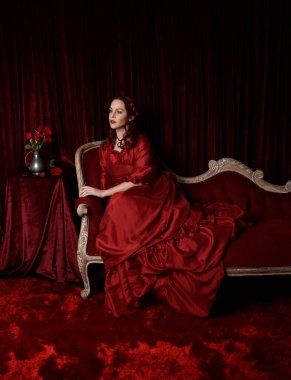  Kızıl saçlı güzel bir kadın modelin portresi Viktorya dönemi kırmızı balo elbisesi giyiyor. Huysuz, karanlık bir geçmişi olan poz vermek..