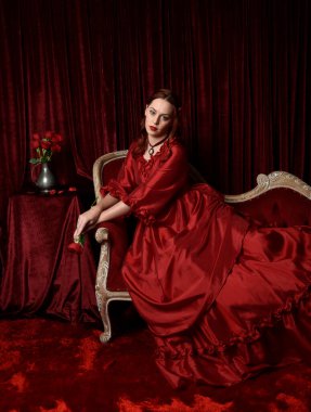  Kızıl saçlı güzel bir kadın modelin portresi Viktorya dönemi kırmızı balo elbisesi giyiyor. Huysuz, karanlık bir geçmişi olan poz vermek..