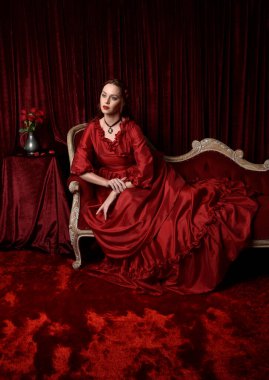  portrait of pretty female model with red hair wearing glamorous historical victorian red ballgown.  Posing with a moody dark background. clipart