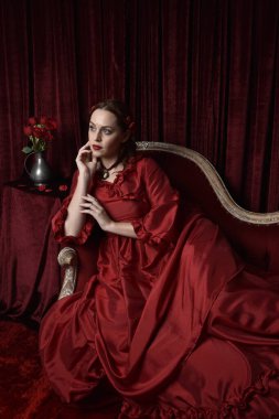  Kızıl saçlı güzel bir kadın modelin portresi Viktorya dönemi kırmızı balo elbisesi giyiyor. Huysuz, karanlık bir geçmişi olan poz vermek..