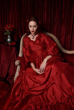  Kızıl saçlı güzel bir kadın modelin portresi Viktorya dönemi kırmızı balo elbisesi giyiyor. Huysuz, karanlık bir geçmişi olan poz vermek..