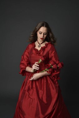  Kızıl saçlı güzel bir kadın modelin portresi Viktorya dönemi kırmızı balo elbisesi giyiyor. Huysuz, karanlık bir geçmişi olan poz vermek..