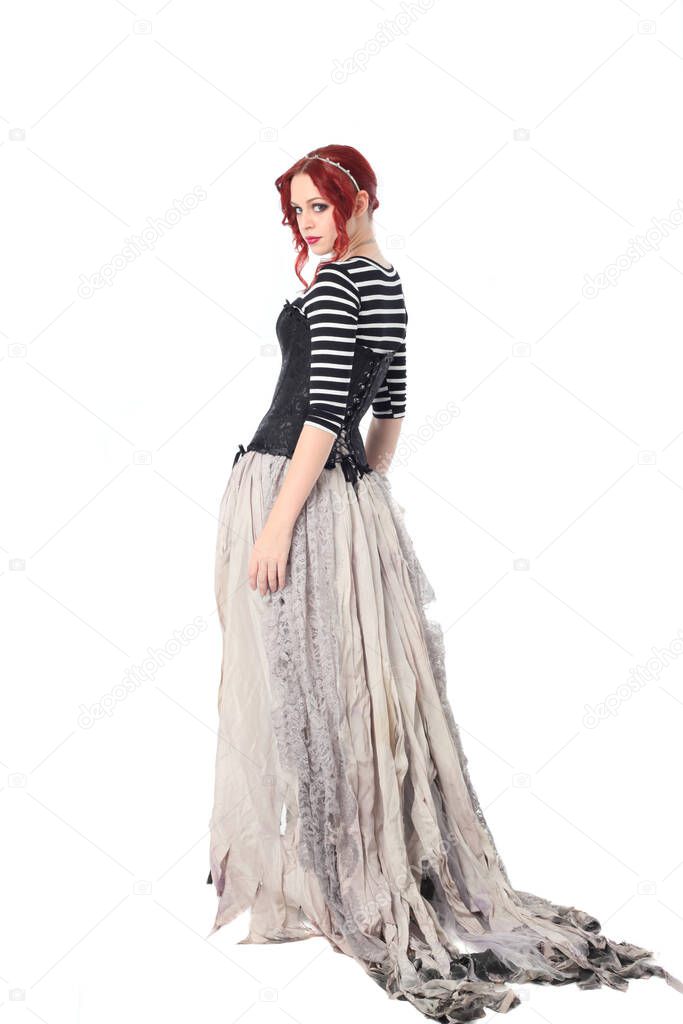 full length portrait of girl with red hair wearing black corset , torn gothic fantasy gown and leather boots. standing pose, isolated on white studio background.