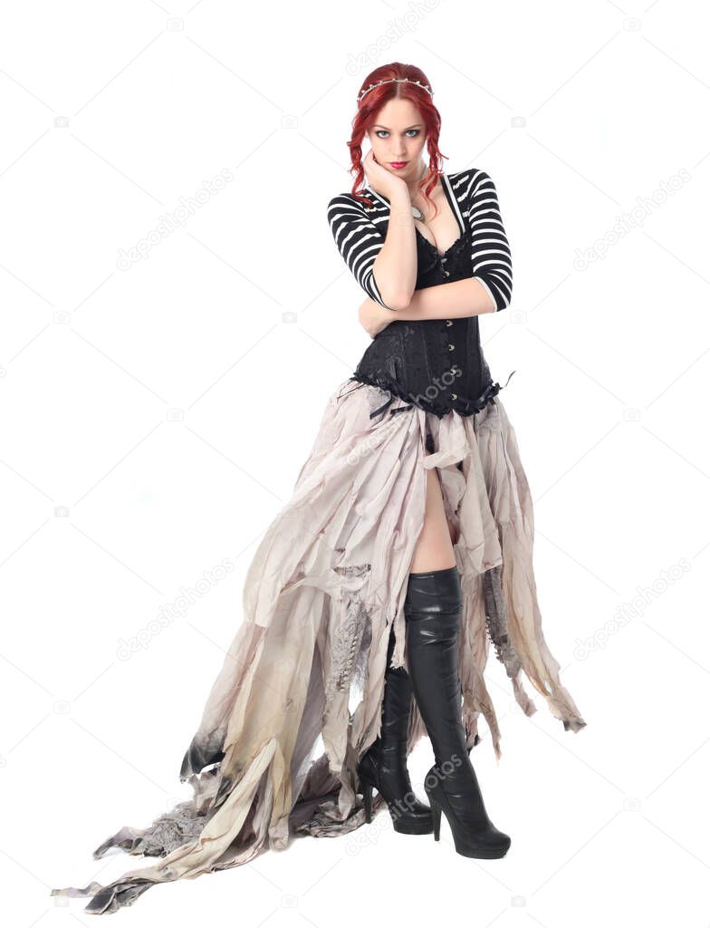 full length portrait of girl with red hair wearing black corset , torn gothic fantasy gown and leather boots. standing pose, isolated on white studio background.