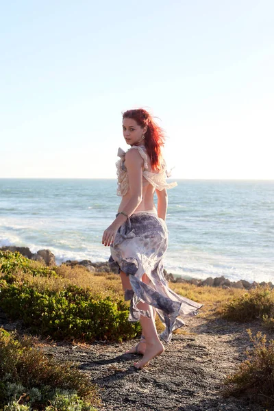 portrait of pretty female ship wrecked  model wearing  torn dress.  posing on the rocky  Ocean shoreline at sunset,