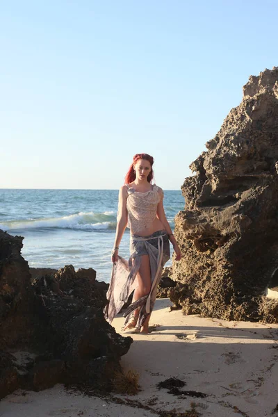portrait of pretty female ship wrecked  model wearing  torn dress.  posing on the rocky  Ocean shoreline at sunset,