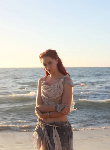 portrait of pretty female ship wrecked  model wearing  torn dress.  posing on the rocky  Ocean shoreline at sunset,